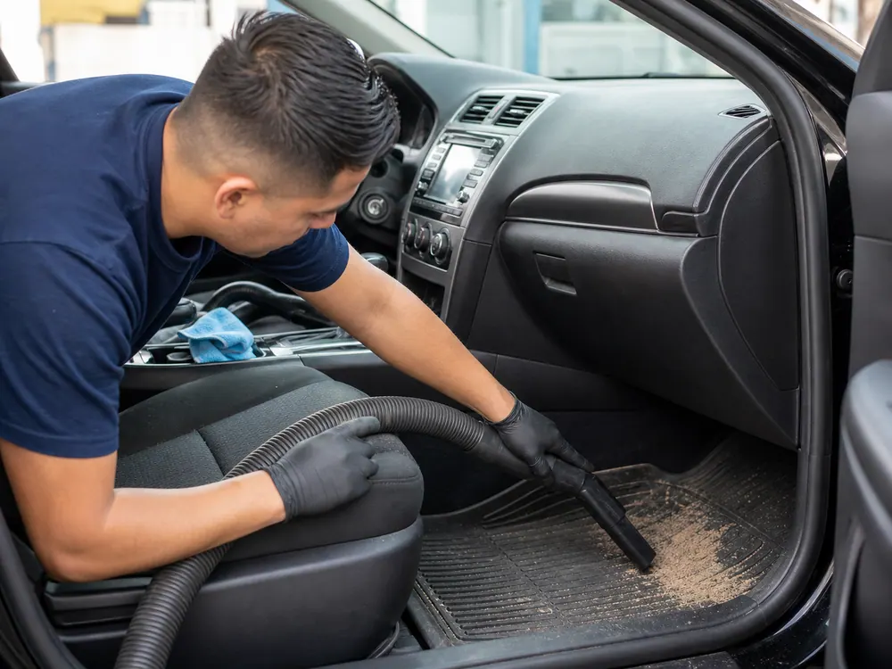 Worker vacuuming sand from a family SUV footwell after a South Bay beach weekend.